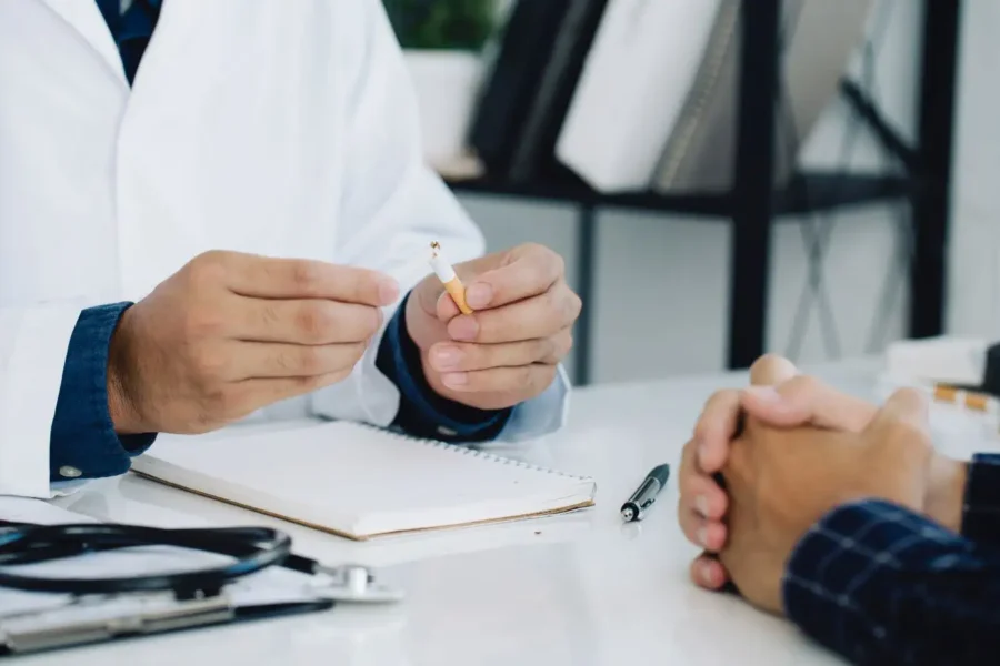 Consultation avec un professionnel de santé discutant de l'arrêt du tabac, avec une cigarette cassée en symbole de sevrage.